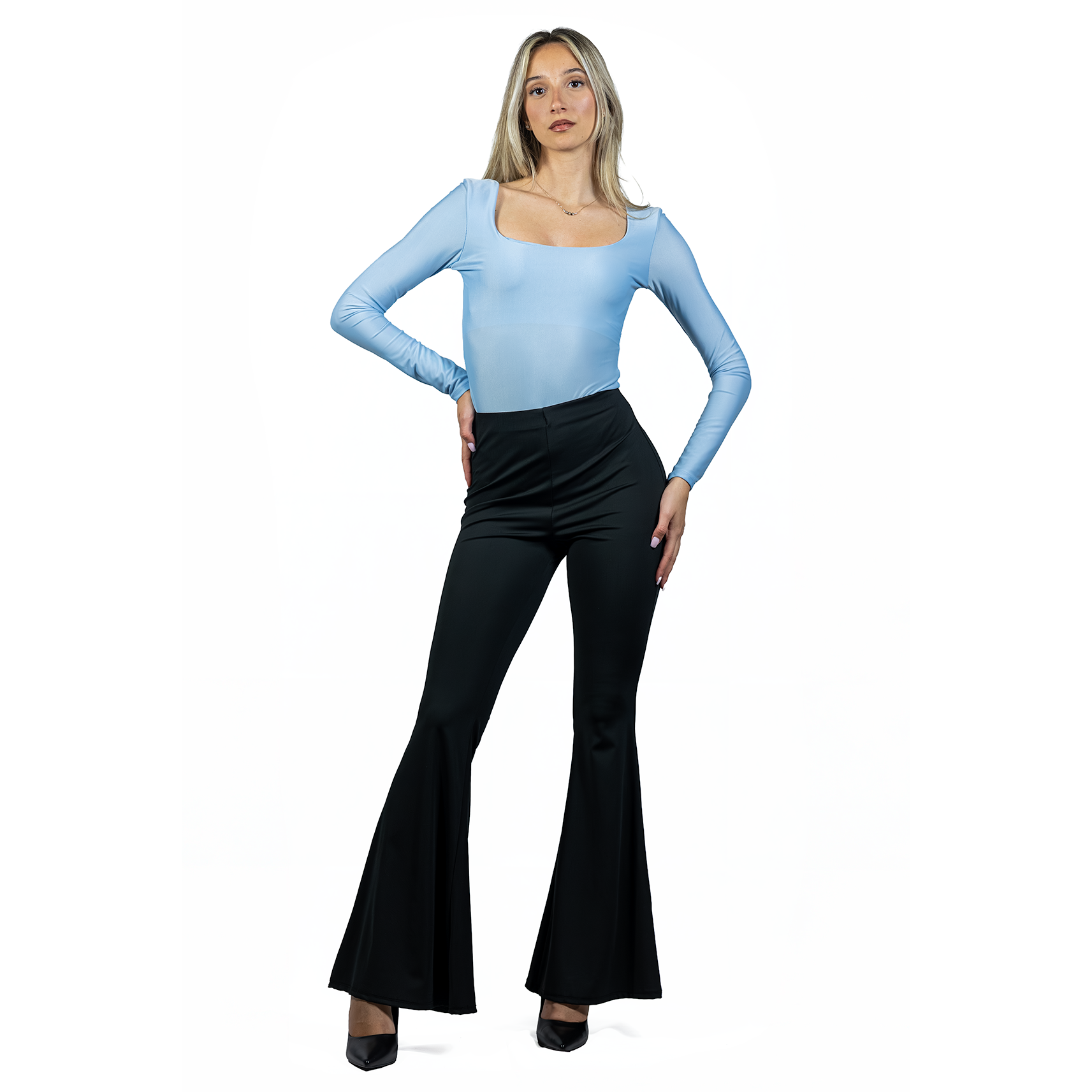 A woman stands confidently wearing a light blue long-sleeve top, black FLARE PANT in stretch fabric with a high waist, and black heels, posed against a white background.