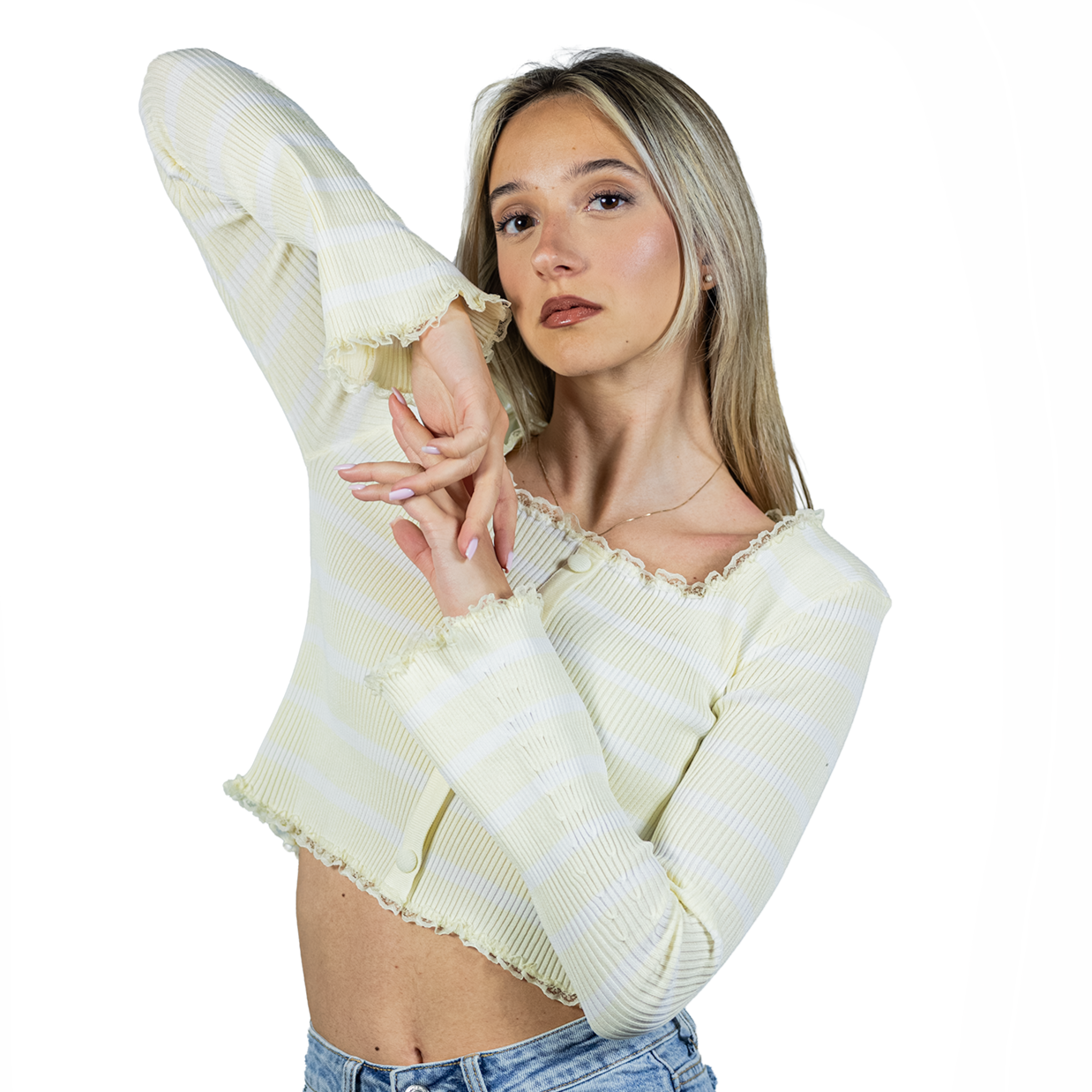 A young woman with light hair poses with one arm raised, wearing the MAGLIA LUME', a light yellow and white striped cropped ribbed top with bell sleeves, paired with blue jeans against a white background.